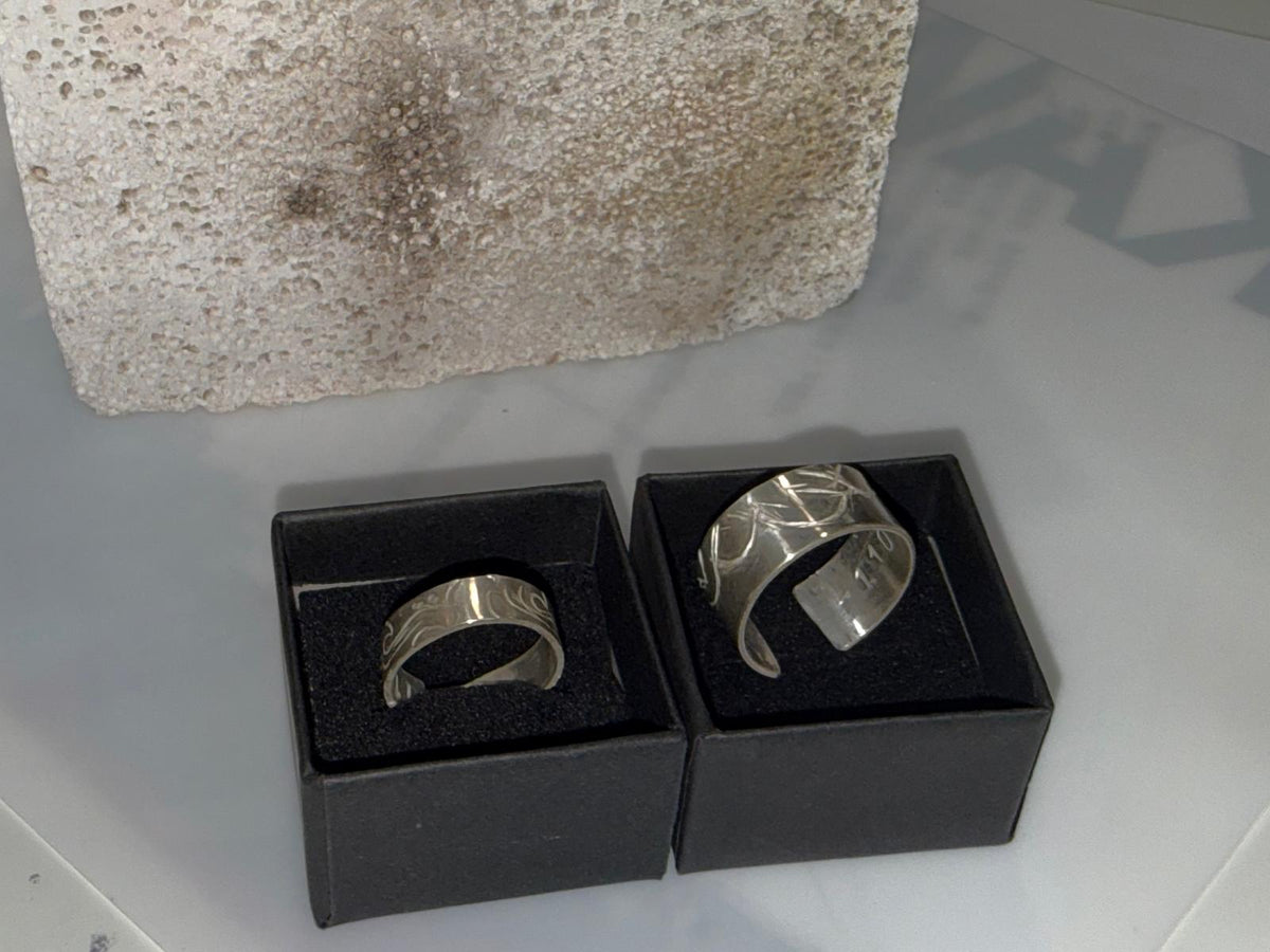 Two patterned silver rings displayed in boxes